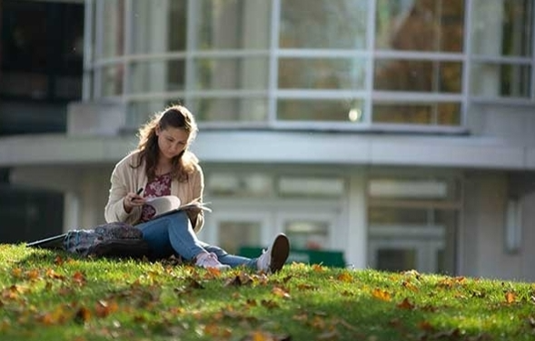 Female student studying on grassy hill at Illinois Wesleyan University.